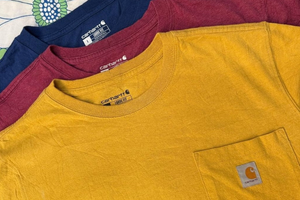 Three folded t-shirts in blue, red, and yellow with Carhartt logos.
