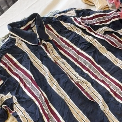 Unboxing a 25kg wholesale bag of men’s short sleeve shirts, showcasing a variety of second hand and vintage shirts including patterned, plain, and branded pieces.

