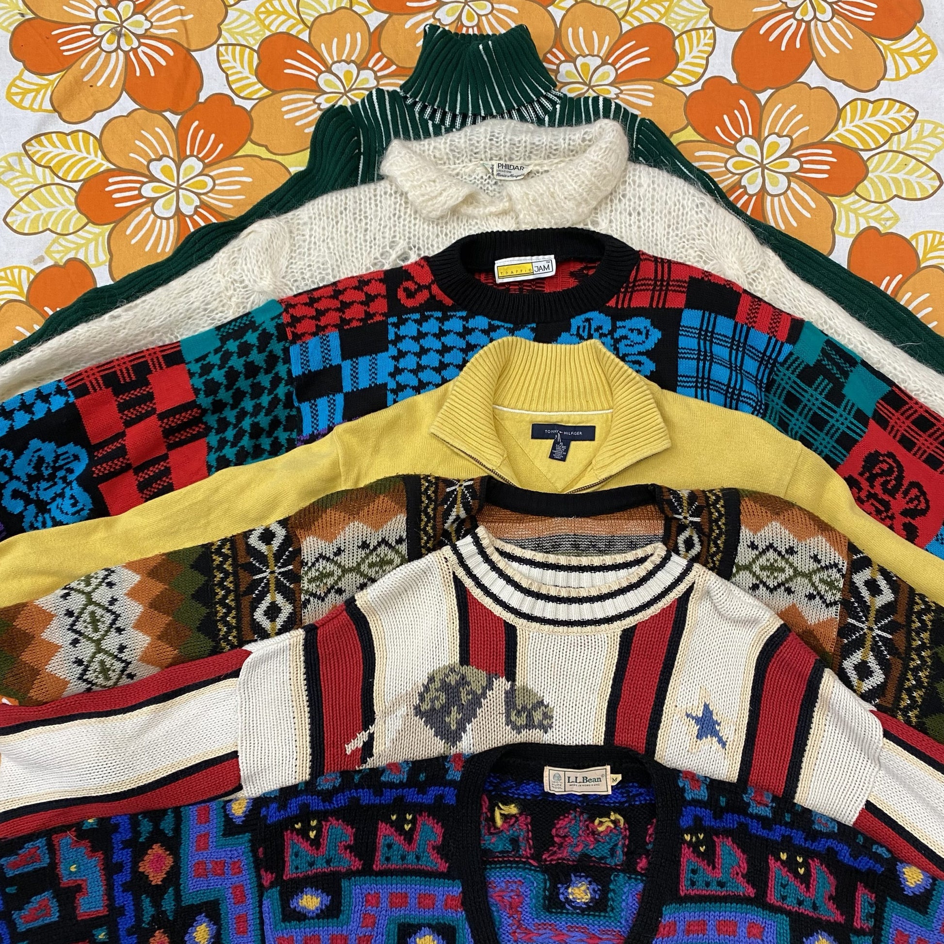 Collection of colorful patterned sweaters on hangers against a floral background