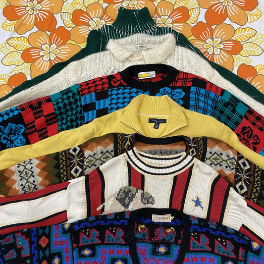 Collection of colorful patterned sweaters on hangers against a floral background
